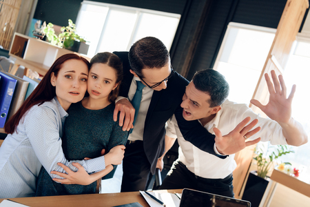 Family lawyer is holding back invasive adult man who is trying to hit restless wife with daughter. Dissolution of marriage of two adults. Two parents fighting over child in divorce concept.の写真素材
