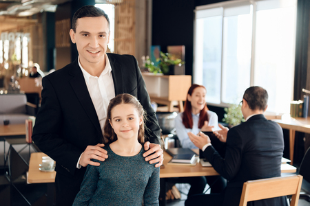 Joyful adult man is standing in foreground and hugging joyful girl in lawyer's office. Family in office of family lawyer.の写真素材