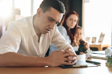 Stunned man, with folded arms, sits at table next to agitated woman hugging girl in lawyer's office. Adult couple is divorced.の写真素材
