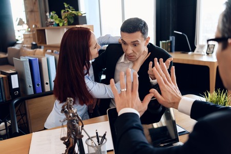 Enraged wife strangles astonished husband, sitting at divorce lawyer's table. Adult couple is...