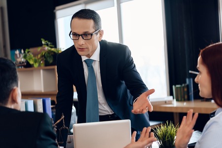 Divorce lawyer points hand at redhead woman next to man sitting in office. Back view. Divorcing couple dissolves marriage contract.の写真素材