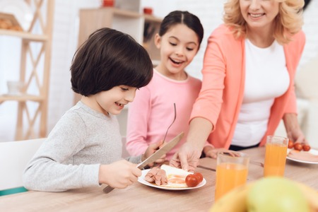 Little grandson with sister watching at eggs with sausages and tomatos on plate. Grandmother prepared dinner for her grandchildren.の写真素材