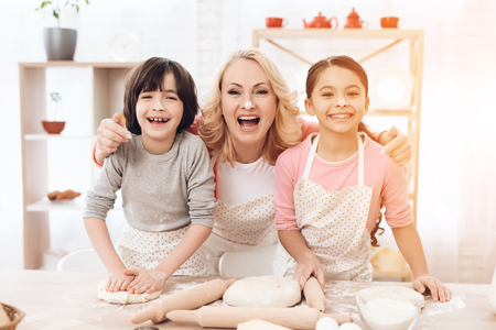 Young grandmother with small grandchildren is laughing in kitchen. Noses dirty with flour. Grandmother has fun with her grandson and granddaughter in kitchen.の写真素材