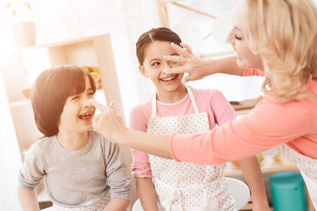 Attractive grandmother smeared with flour nose of a joyful grandson and granddaughter in kitchen. Baking cookies. Beautiful grandmother with her grandchildren bake cookies in kitchen.の写真素材