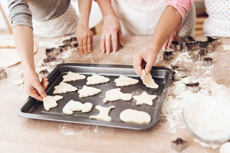 Women's and children's hands lay out cookie biscuits for deco in kitchen. Grandchildren help grandma to cook pastries in kitchen.の写真素材