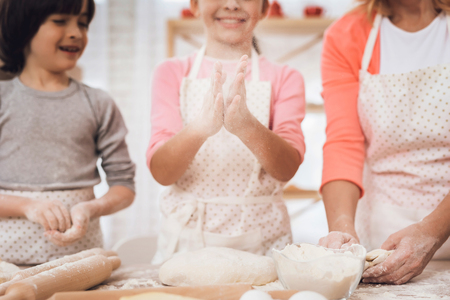 Beautiful grandmother with small grandchildren is laughing in kitchen. Noses dirty with flour. Grandmother has fun with her grandson and granddaughter in kitchen.の写真素材