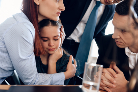 Young red-haired woman hugging crying girl. Man in suit tries to calm mother and daughter. Registration of guardianship of little girl.の写真素材