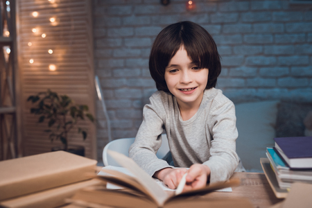 Boy is doing homework surrounded by books at table at night at home.の写真素材