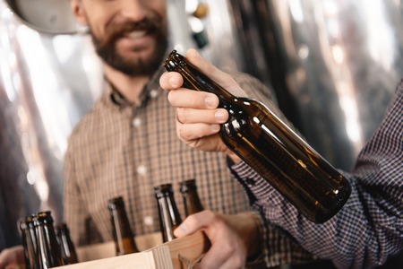 Brewer holds empty beer bottle in hand. Stages of brewing production. Process of beer manufacturing....