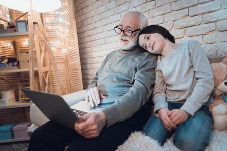 Grandfather and grandson are talking on laptop with family sitting on couch at night at home.の写真素材