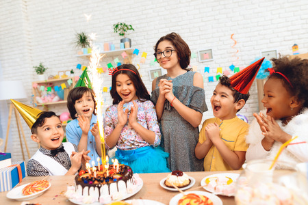 Group of children rejoice of cake with burning candles on occasion of birthday. Birthday concept. Happy children have fun on celebration.の写真素材