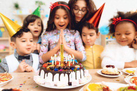 Group of children rejoice of cake with burning candles on occasion of birthday. Little children on...