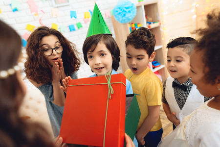 Joyful birthday boy in festive hat receives gift from little girl at birthday party. Happy birthday party. Little children on birthday celebrations.の写真素材