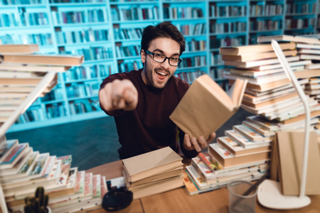 White guy sitting at table surrounded by books in library. Student is emotionally reading book.
