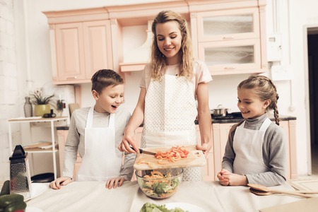 Children with mother at kitchen table in kitchen. Mother is making salad and kids are watching.の写真素材