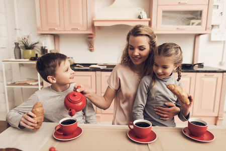 Children with mother at kitchen table in kitchen. Family is drinking tea with croissants.の写真素材