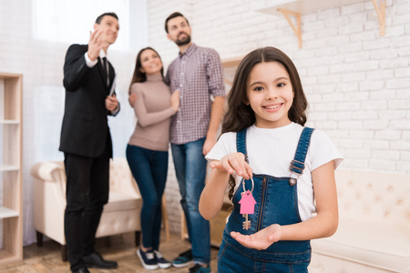 Little girl holds keys to house while realtor shows apartments to young couple. Buying real estate concept.の写真素材