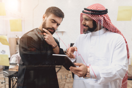 Two arab men in thawb working in office. Coworkers are taking notes in front of glass board.の写真素材