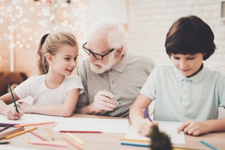 Grandfather, grandson and granddaughter at table at home. Children are drawing with color pencils.の写真素材