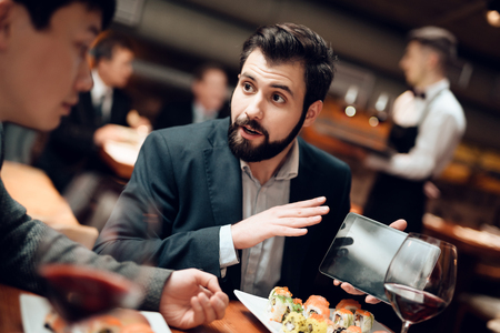 Meeting with chinese businessmen in suits in restaurant. Man is showing tablet.の写真素材
