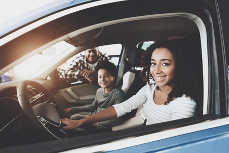 African american family at car dealership. Father, mother and son in new blue car, smiling.