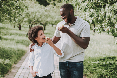 Father with son eat apples in park. Family relations concept.の写真素材