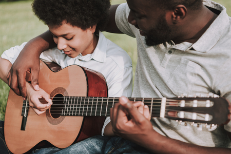 Father and son in the park playing guitar sitting on the grass. Parents and children relationship concept.の写真素材