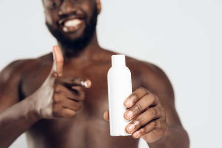 African American smiling man holding aftershave lotion. Isolated on white background. Studio portrait. Male beauty concept.の写真素材