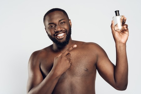 African American man uses aftershave lotion. Male hygiene. Morning hygiene procedures. Isolated on white background. Studio portrait.の写真素材