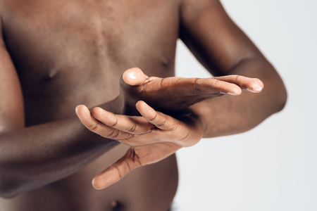 African American man smears hands by moisturizing cream. Hand care. Male beauty concept. Isolated on white background.の写真素材