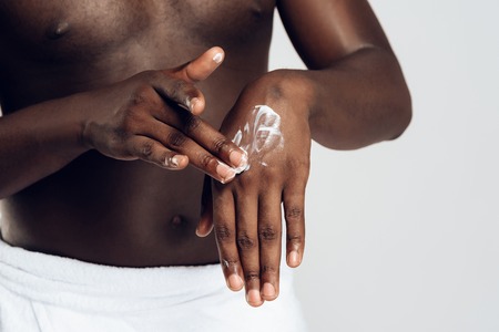 African American man smears hands by moisturizing cream. Hand care. Male beauty concept. Isolated on white background.の写真素材