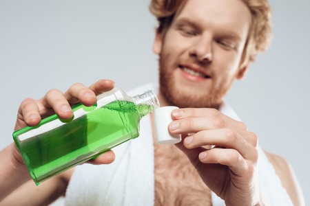 Top view. Red haired man pours mouthwash into cap. Morning hygiene procedures. Isolated on grey background. Studio portrait.の写真素材