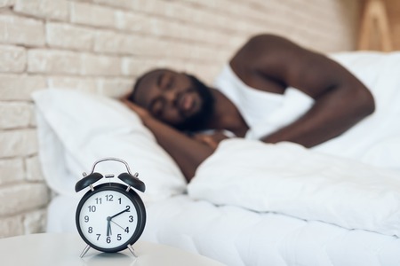 African American man sleeps in bed next to alarm clock. Healthy sleep. Sweet dreams.の写真素材