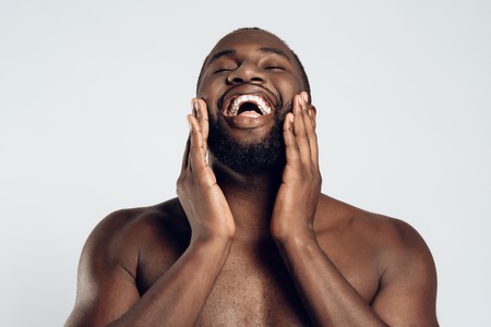African American smiling man is smeared with face cream. Face care. Morning hygiene procedures. Isolated on white background. Studio portrait.の写真素材
