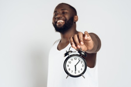 African American smiling man posing with alarm clock in hands. Time is running. Clock is ticking. Isolated on white background. Studio portrait.の写真素材