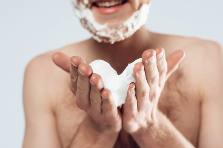 Young red haired guy smears shaving cream on stubble. Male hygiene. Male beauty concept. Isolated on grey background. Studio portrait.の写真素材