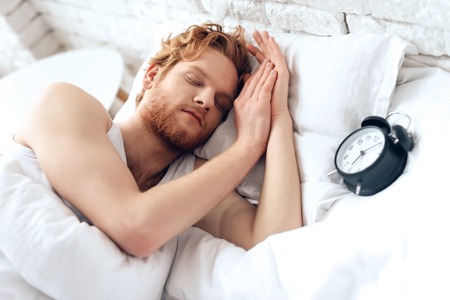 Young hipster sleeps under white blanket. Sweet dreams. Waking up. Healthy sleep.の写真素材