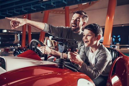 Smiling father and son sitting on toy car. Spending holiday together with family. Entertainment center, mall, amusement park. Family rest, leisure concept.の写真素材