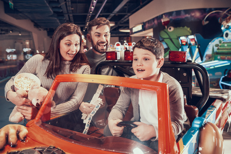 Happy family, enraptured son sitting on toy car. Rest, holiday, leisure. Spending time together. Entertainment center, mall, amusement park.の写真素材
