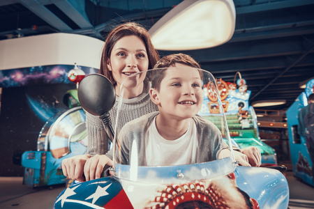 Happy mom and son on toy motorcycle. Family rest, leisure. Spending holiday together with family. Entertainment center, mall, amusement park.の写真素材