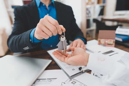 Realtor gives keys to buyer in office at table.