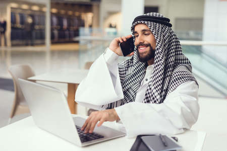 Young Arabian Man Using Phone and Laptop in Cafe.の写真素材