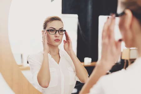Woman looking in mirror and holding on to glasses.の写真素材