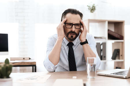 A man with a beard at his desk feels a migraine.の写真素材
