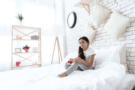 Little girl sitting on a white bed with a sad faceの写真素材