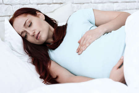A woman with pain lies on the bed and feel pain.の写真素材