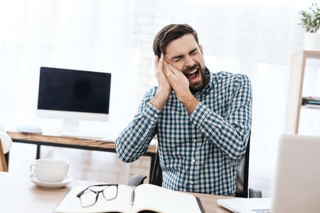A man in shirt sits and screams from severe pain.の写真素材