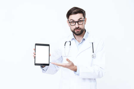 Doctor in a white coat holds a tablet in his handsの写真素材