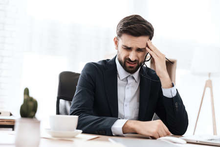 Man in suit suffers from a migraine at workplace.の写真素材