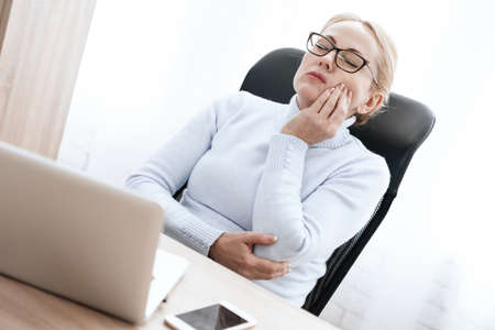 A woman sits at a table while working at computer.の写真素材
